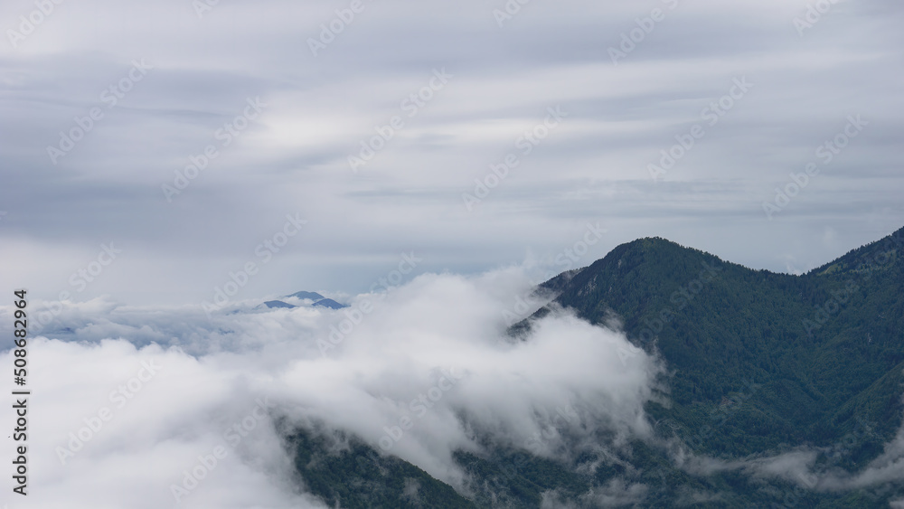 Stunning view of the forested mountain peak with the surrounding mist of Velika Planina, Slovenia