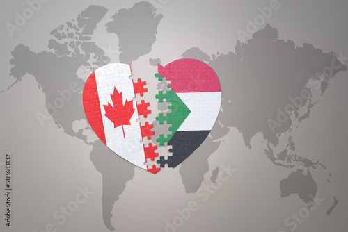 puzzle heart with the national flag of canada and sudan on a world map background.Concept.