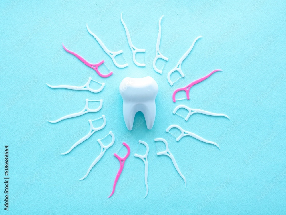 Obraz premium Dental concept of oral hygiene. Dental floss with a white and pink plastic toothpick lie in a circle in the center of a large white tooth