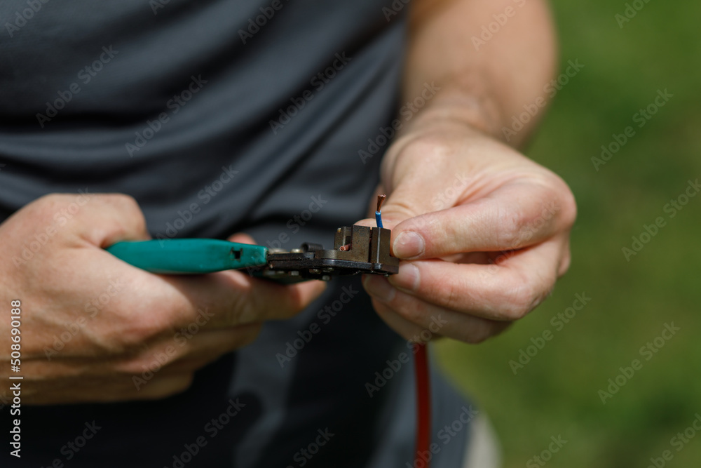 man cutting an electrical cable's insulation with wire strippers