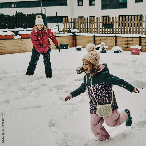 Mother and daughter in snow clothes playing throwing snowballs after a heavy snowfall