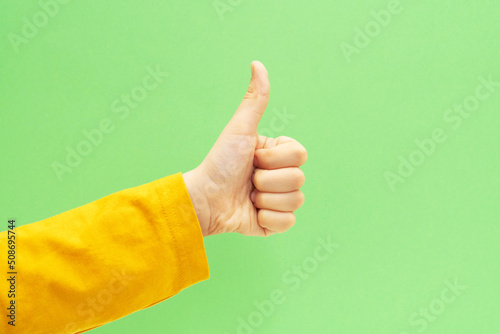 Hand with happy thumb up gesture on green background. Approving expression from child.