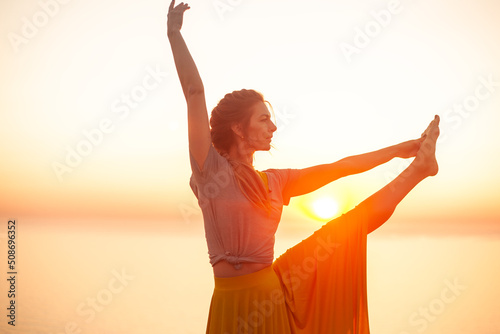 Back view of young woman engaged in yoga in nature with view and warm light of sunset, makes poses enjoy the meditation, balance and sunrise © Вероника Зеленина
