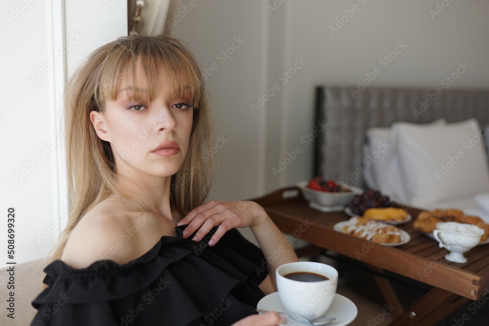 In the photo, the girl is drinking coffee at her balcony. A man takes a picture of her, she is enjoying the morning and breakfast In the photo, the girl is drinking coffee at her balcony. A man takes a picture of her, she is enjoying the morning and breakfast