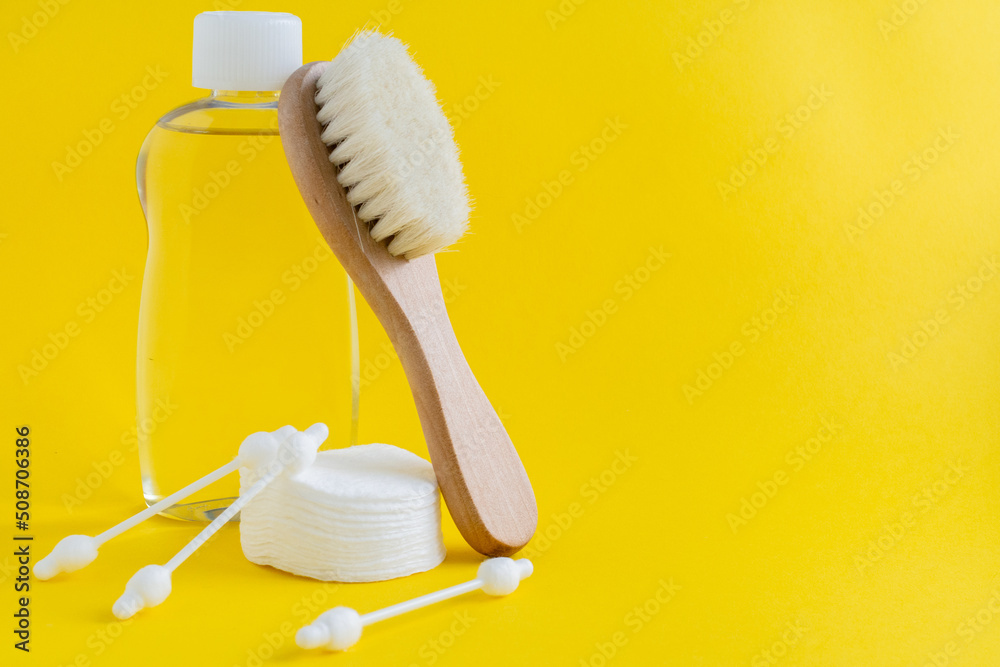 Wooden hair brush, bottle of baby cosmetic product, cotton ear sticks and cotton pads on yellow background. Composition of baby cosmetics.Image for sites about babies and baby cosmetic products. 