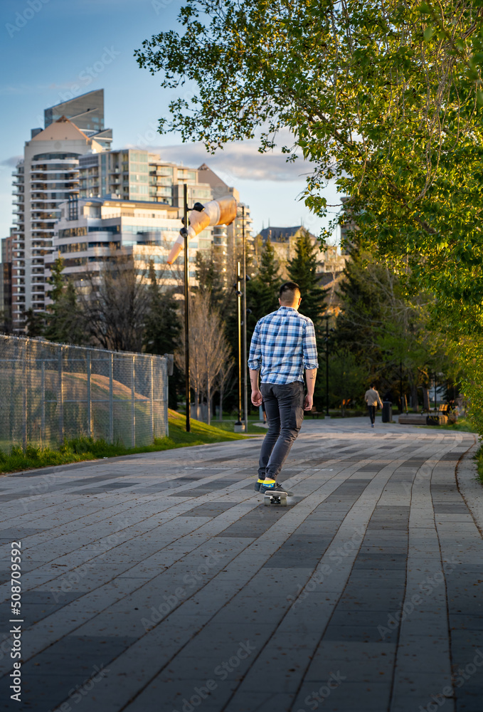 Calgary Alberta Canada, May 16 2022: A young man rides a skateboard down a downtown walkway during a summer evening near Princess Island Park.