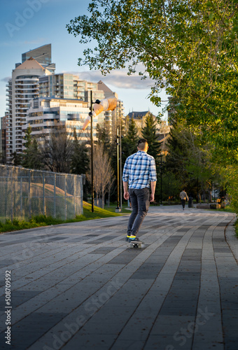 Calgary Alberta Canada, May 16 2022: A young man rides a skateboard down a downtown walkway during a summer evening near Princess Island Park.