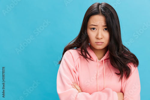 Upset sad cute Asian student young lady in pink hoodie sweatshirt folds hands posing isolated on over blue studio background. The best offer for ad. People Emotions for Everyday concept © SHOTPRIME STUDIO