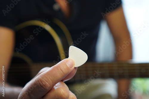 Caucasian man shows fist satisfied with his improvements playing the guitar  shows plethrus in the foreground