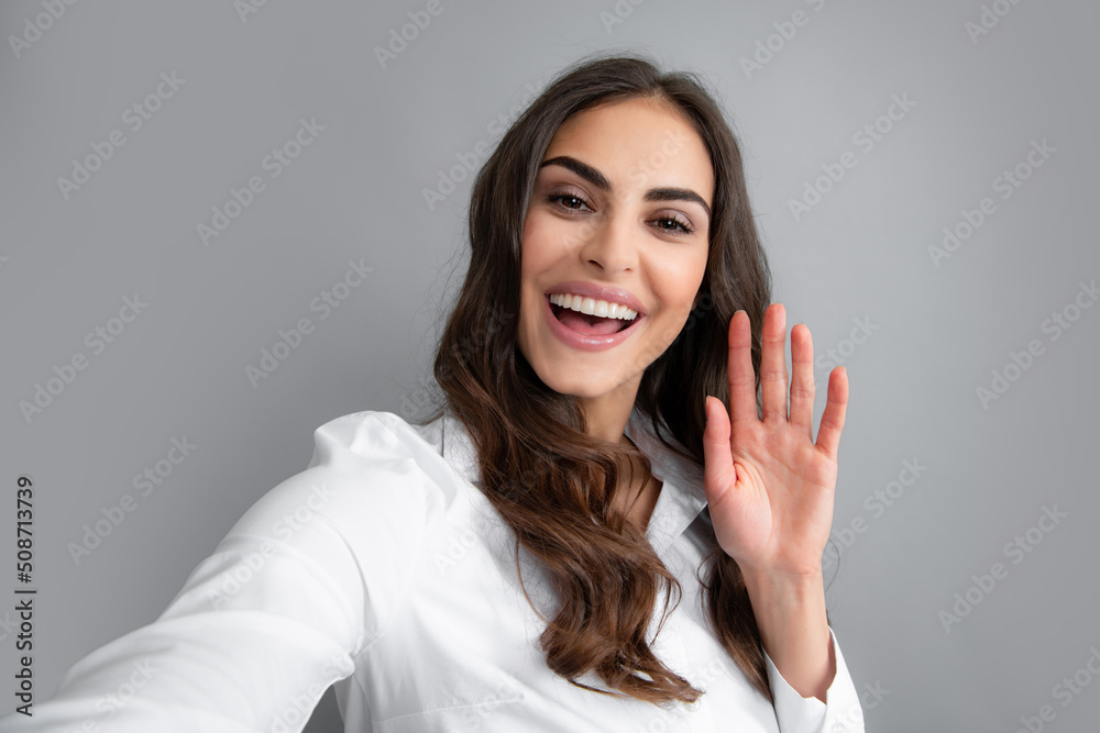 Photo of beautiful brunette woman laughing and taking selfie photo on cellphone isolated over gray background. Photo of beautiful brunette woman laughing and taking selfie photo on cellphone isolated over gray background.