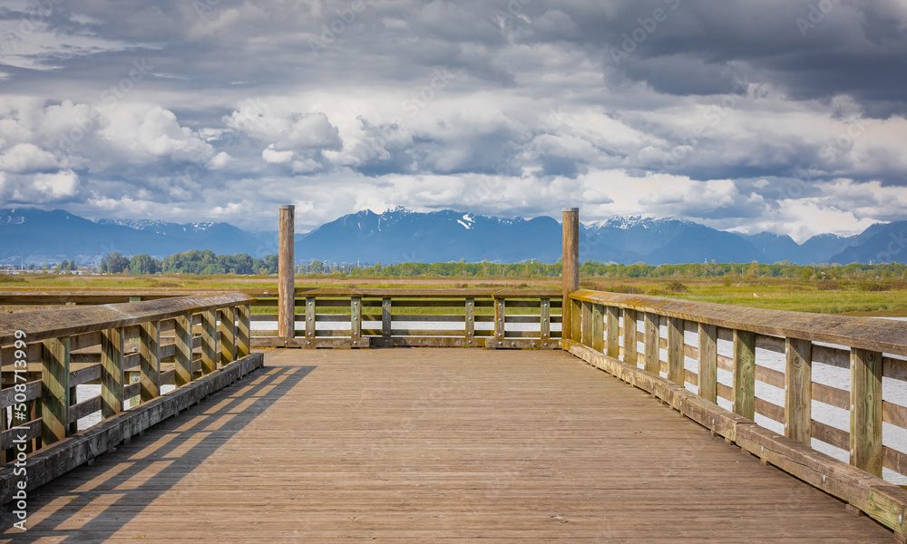 Perspective view of a wooden pier on a river and beautiful mountains at the backgrond.