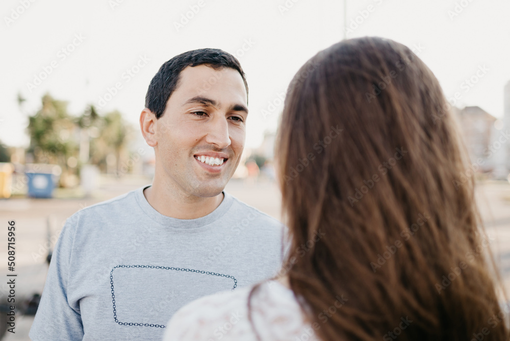 A Hispanic stylish man is staring at his kind brunette girlfriend near the pier in Spain in the evening. A couple of tourists on a date in Valencia. A Hispanic stylish man is staring at his kind brunette girlfriend near the pier in Spain in the evening. A couple of tourists on a date in Valencia.