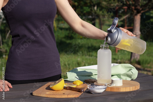 Girl makes a fresh homemade isotonic drink from natural ingredients - salt, lemon and mineral water