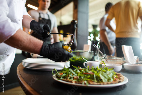 The chef sprinkles olive oil on the finished pizza