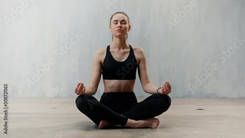 Young healthy woman in black sportsclothes practising yoga in studio, in a yoga position, copy space