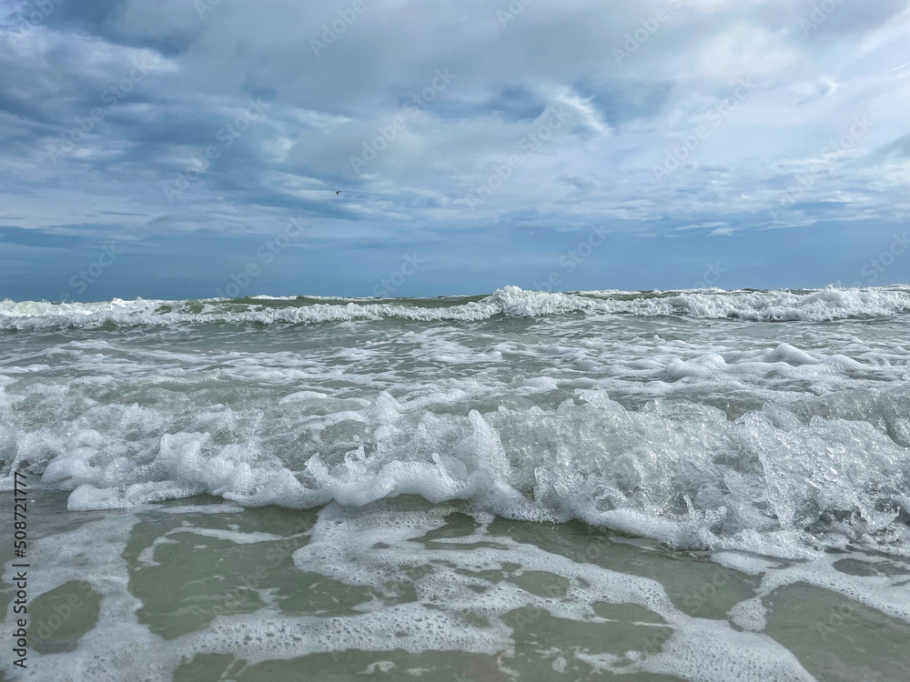 Fototapeta premium Meer mit Wellen aus der Sicht von der Küste mit bewölktem Himmel