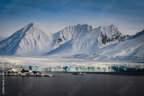 Foto 2022-05-13 SNOW COVERED MOUNTAIN RANGE WITH A GLACIER AND CALM ARCTIC OCEAN AND