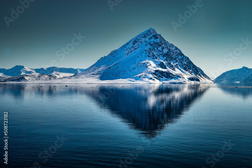 202-05-12 ARCTIC WITH ONE A SHAPED MOUNTAIN WITH SNOW AND EXPOSED ROCK WITH ITS REFLECTION N THE WATER AND A CLEAR SKY NEAR THE ISLAND OF SVALBARD IN NORWAY