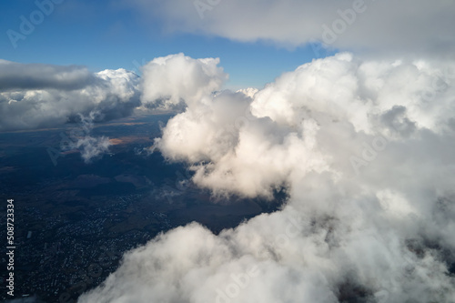 Aerial view from airplane window at high altitude of earth covered with puffy cumulus clouds forming before rainstorm © bilanol