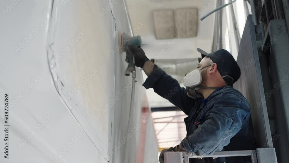 A production line worker in a respirator is sanding the car wall before finishing painting using a mechanical sander. Dusty work in the paint shop of the wagon plant A production line worker in a respirator is sanding the car wall before finishing painting using a mechanical sander. Dusty work in the paint shop of the wagon plant