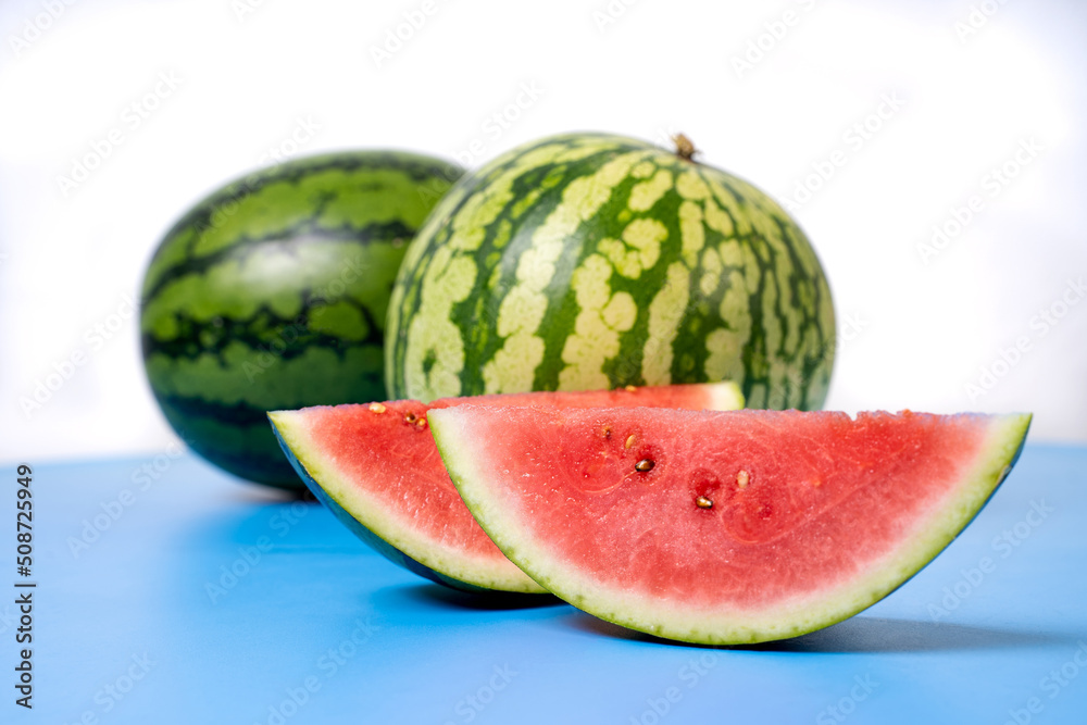 Two whole watermelons and a watermelon cut into smaller pieces. Watermelons with green skin colour and red flesh inside on a white background.