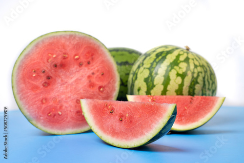 Two whole watermelons and a watermelon cut into smaller pieces. Watermelons with green skin colour and red flesh inside on a white background.