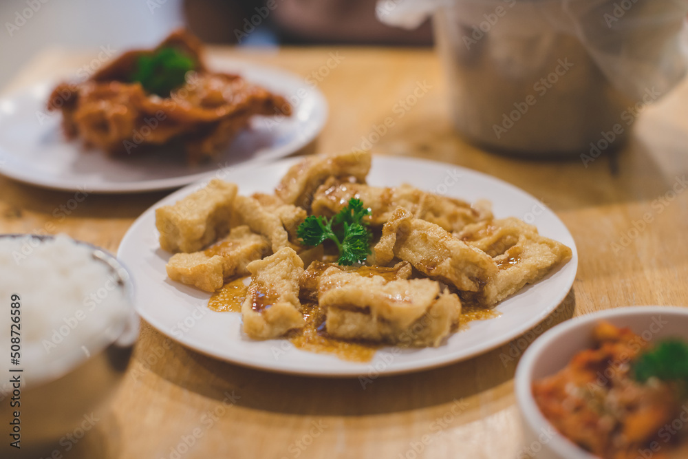 Fried tofu topping with japanese sauce on white plate with dinner meal background Fried tofu topping with japanese sauce on white plate with dinner meal background