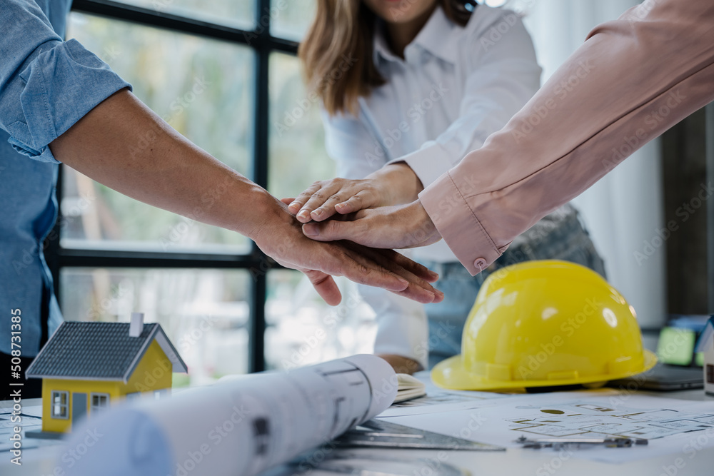 Close up of hands are working on home model mock-up, plan drawings, engineer and architectural tools, paperworks that show architectural, engineering, and work details.