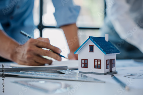 Close up of hands are working on home model mock-up, plan drawings, engineer and architectural tools, paperworks that show architectural, engineering, and work details.