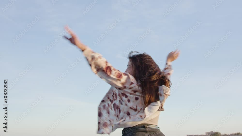 Medium shot young happy woman smiling and spinning on the beach with her arms in the air