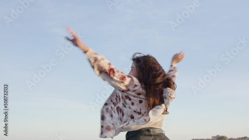 Medium shot young happy woman smiling and spinning on the beach with her arms in the air