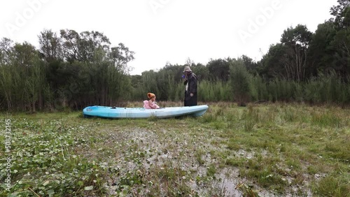 A man in a trenchcoat drinks tea out in a swamp with his daughter in a kayak. photo