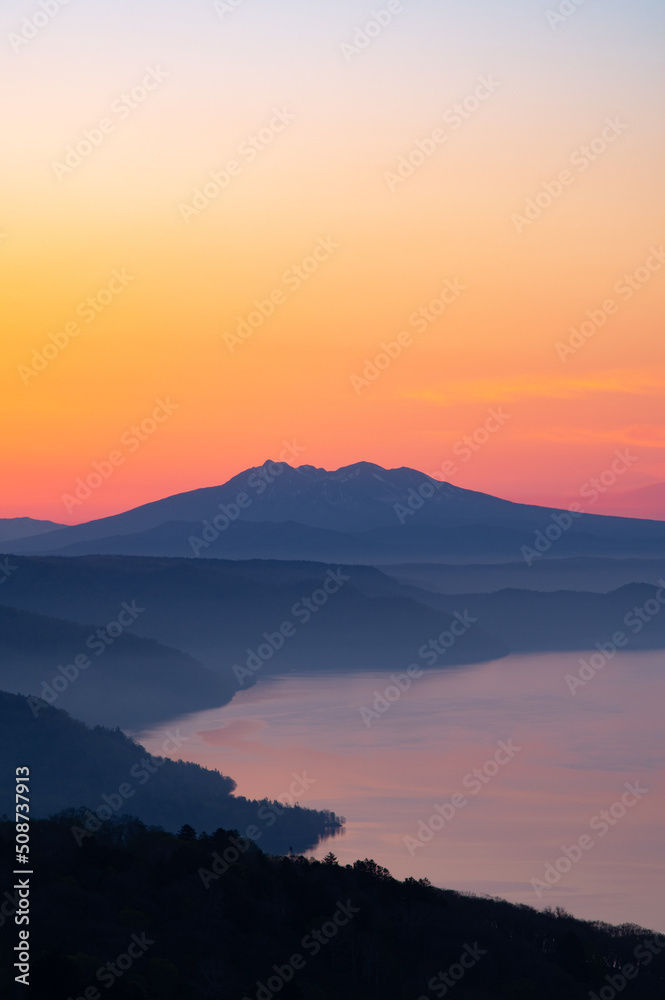 湖を見下ろす夜明けの空と遠くの山のシルエット。日本の北海道の美幌峠の風景。