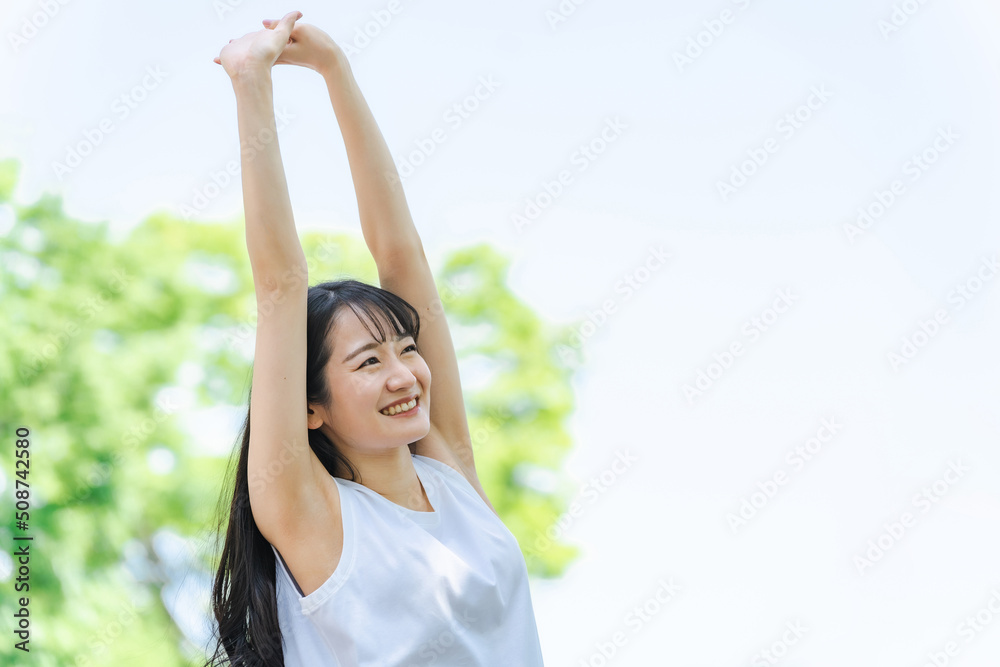 新緑の中でストレッチをする女性（健康・笑顔）
