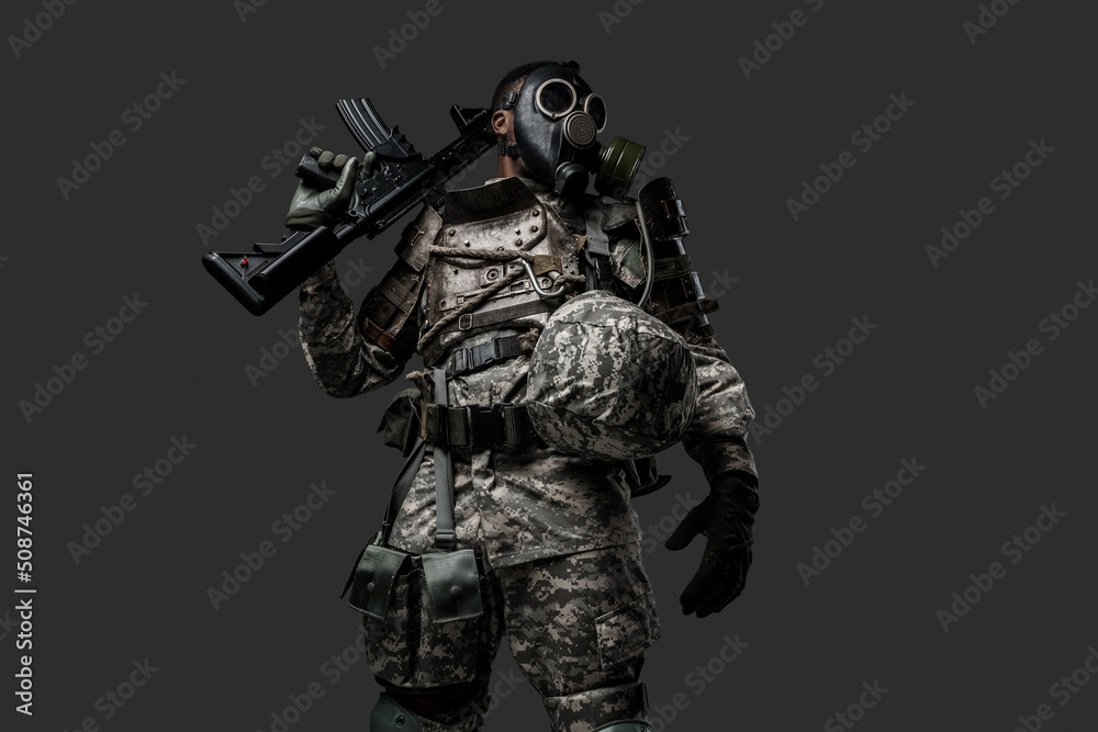 Studio shot of black military man holding rifle on his shoulder isolated on grey background.