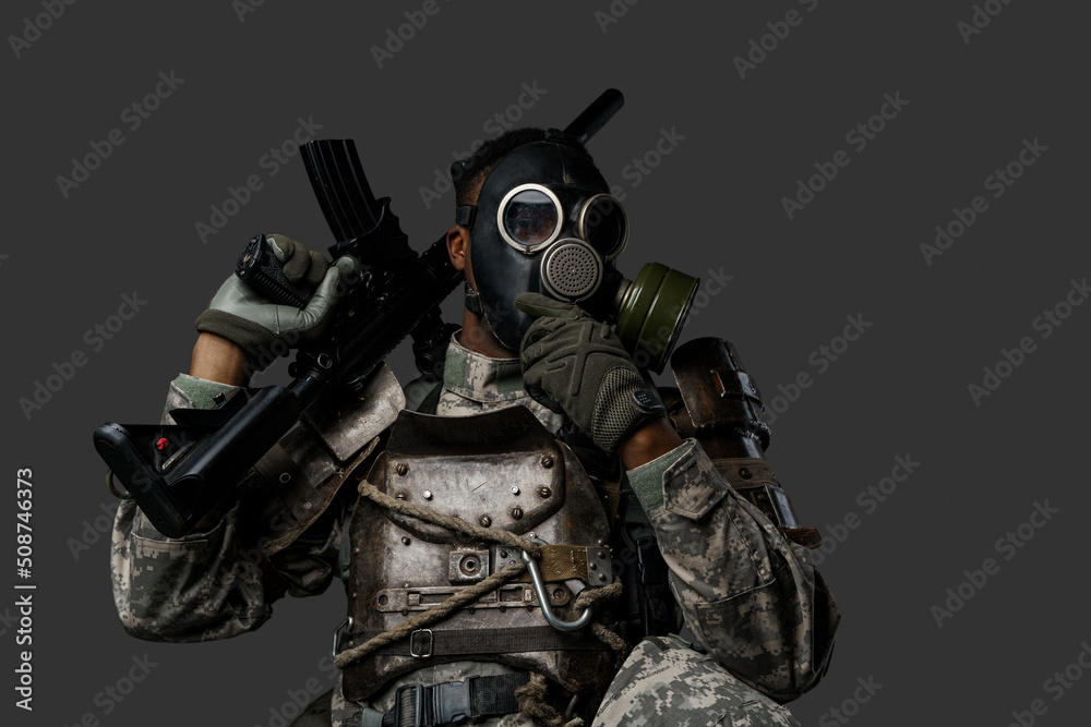 Studio shot of black military man with gas mask holding rifle on his shoulder looking at camera.