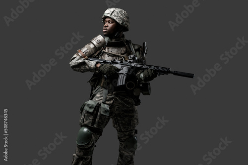 Photo of isolated on grey black soldier dressed in protective uniform posing with rifle.
