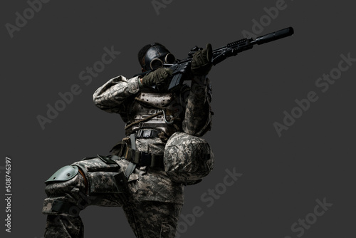 Studio shot of black military man with gas mask aiming rifle isolated on grey background.