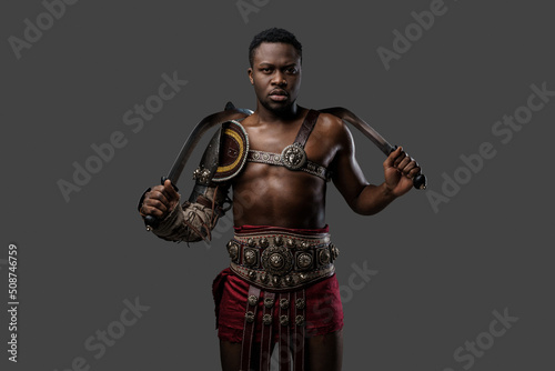 Shot of antique gladiator of african descent holding dual swords isolated on gray background.
