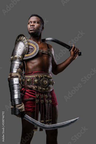 Shot of ancient gladiator of african ethnic holding twin swords isolated on gray background.