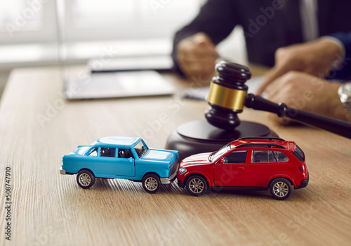 Little crashed autos on table in courtroom. Gavel and two small toy car models on desk in courthouse. Concept of lawyer services, civil court trial, vehicle accident case study, and insurance coverage photo