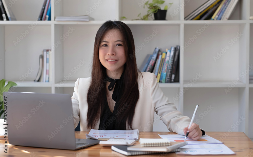 Charming Asian woman working at the office using a laptop Looking at the camera. Charming Asian woman working at the office using a laptop Looking at the camera.