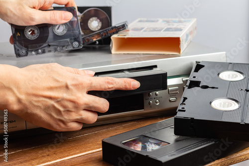 Canvas-taulu hand holds magnetic audio tape cassette for music inserts VHS videocassette into