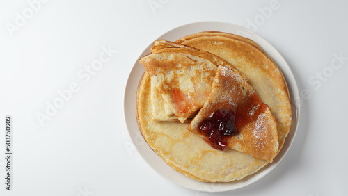 French crepes for Breakfast with strawberry jam.  Wheat golden yeast pancakes or crepes in a white plate closeup.