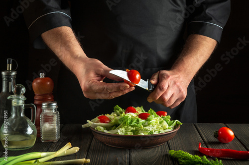 Fototapeta Naklejka Na Ścianę i Meble -  Chef prepares a vegetable salad in the kitchen. Cutting a fresh tomato for a vitamin salad with a knife