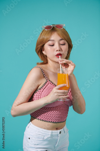 Pretty young happy blonde woman isolated over turquoise background holding orange juice cup drinking and enjoying