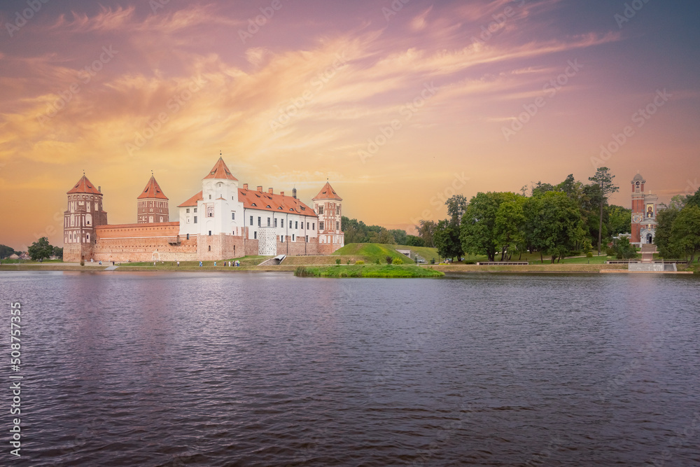 Mir Castle landmark on river against backdrop of sunset sky