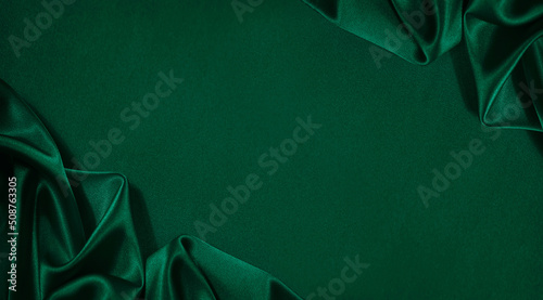 Dark green silk satin background. Wavy folds. Smooth surface. Shiny fabric. Luxury background with copy space for design. Web banner. Top view table. Flat lay. Wide. photo