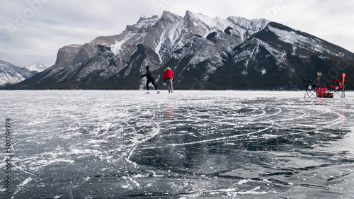 Man and woman wild skating on a frozen alpine lake under a big mountain , Banff N. Park, Canada