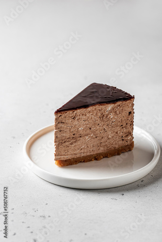 A piece of chocolate cheesecake on a white plate on white background. Text space